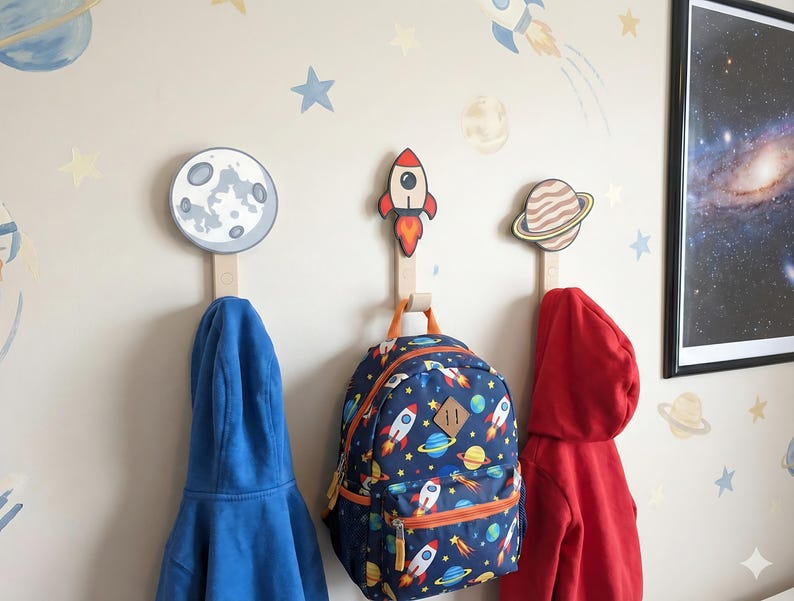 Moon, rocket, and Saturn wall hooks holding children’s clothes and a space-themed backpack